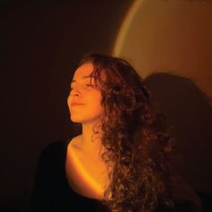 a woman with long curly hair standing in front of a wall and looking off into the distance