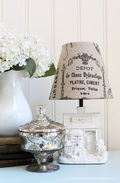 a table with a lamp, vase and flowers on it