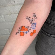 a person with a tattoo on their arm holding a bowl of oranges and flowers