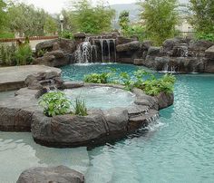 an outdoor pool with waterfall and water features surrounded by large rocks, plants and trees