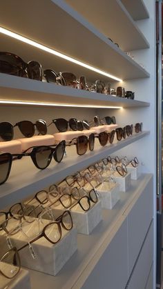 many pairs of sunglasses are on display in a store window, with white shelves holding them