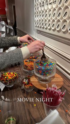 two people cutting into a cake with candy on the table next to it and another person holding a knife