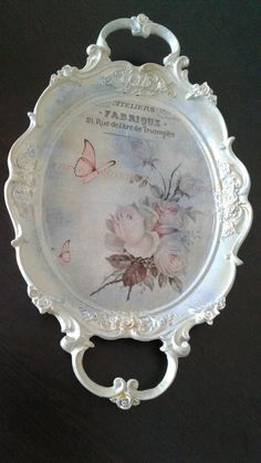 an ornate silver plate with flowers and butterflies painted on the side, sitting on a black surface