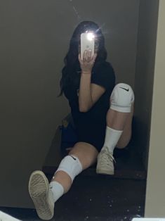 a woman sitting on the stairs taking a selfie with her cell phone and knee braces