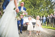 a bride and groom standing next to their flower girls in front of the wedding car