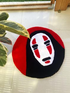 a red and black rug with a face on it next to a potted plant