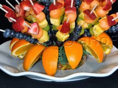 an arrangement of fruit is arranged on a platter with toothpicks and oranges