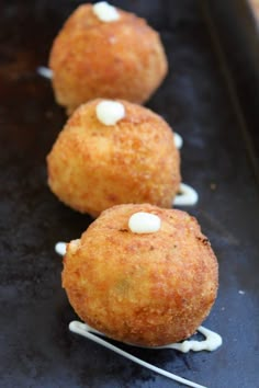 three fried food items sitting on top of a black tray with toothpicks sticking out of them