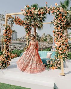 a woman in an orange and white wedding dress standing under a floral arch with flowers on it