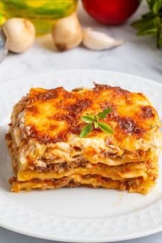 a white plate topped with lasagna covered in cheese and sauce next to garlic