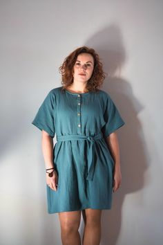 a woman standing in front of a white wall wearing a green dress and black shoes