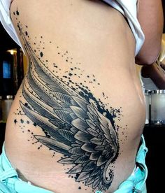 a woman's stomach with an angel wing tattoo on her belly and the side