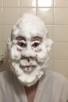 a man with foam on his face in front of a bathroom mirror and tiled wall