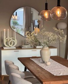 a wooden table topped with a vase filled with flowers next to two lights hanging from the ceiling