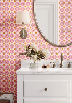 a bathroom with pink and orange wallpaper, white cabinets and a round mirror on the wall