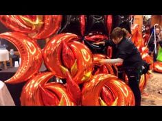 a woman standing next to a pile of red foil balloons in front of a wall