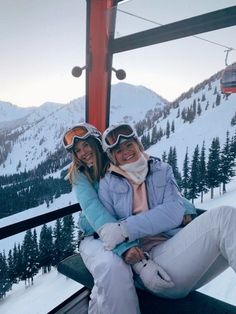 two women sitting on a ski lift in the snow with their arms around each other