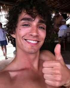 a shirtless young man giving the thumbs up sign with his right hand and smiling