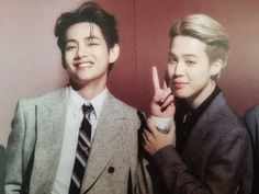 two young men standing next to each other in front of a wall with one holding the peace sign