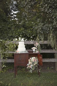 a wedding cake sitting on top of a table next to a wooden bench covered in greenery