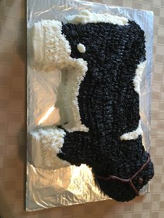 a cake shaped like a cow on top of a sheet of tin foil with white and black frosting