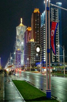 a city street at night with tall buildings in the background