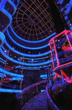 the inside of a building with blue and red lights on it's ceiling, along with spiral staircases