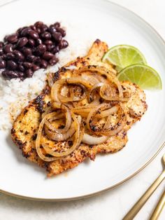 a white plate topped with chicken, rice and beans next to a lime wedge on top of a table