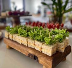 a wooden tray filled with lettuce on top of a white table next to other food