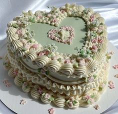 a heart shaped cake on a white plate with pink and green flowers around the edges