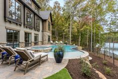 an outdoor swimming pool with lounge chairs and trees in the background, next to a house