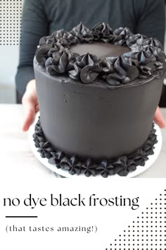 a black frosted cake sitting on top of a white plate next to a person