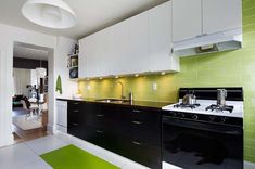 a kitchen with black and white appliances and green tiles on the wall, along with an area rug