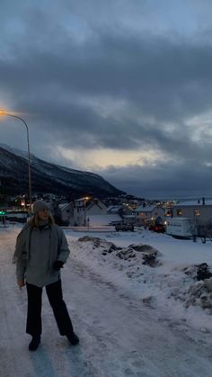 a woman standing in the middle of a snow covered road at night with mountains in the background