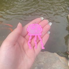 a hand holding a pink beaded object in front of a pond with goldfish