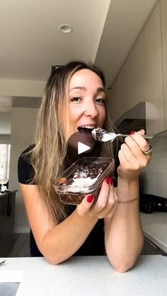 a woman sitting at a kitchen counter eating ice cream and chocolate cake with a spoon in her mouth