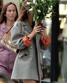 a woman walking down the street with flowers in her hand while holding onto a purse