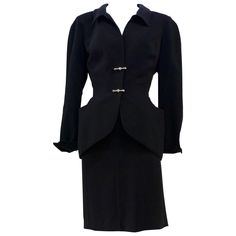 This THIERRY MUGLER skirt suit is composed of a black polyester fabric. Features a classic Mugler silhouette with nipped waist and curved bust-line to neckline design. The jacket has front snap closures, rounded shoulders, and silver and rhinestone hardware detail. The classic pencil style skirt features a zipper closure. In good vintage pre-owned condition. Made in France. Measurements in Inches: Jacket Bust: 38 Waist: 29 Skirt Waist: 26 Hip: 40 Length: 21 Mugler Skirt, Grey Skirt Suit, Mugler Black, Black Skirt Suit, Green Denim Jacket, Rhinestone Skirt, Rounded Shoulders, Evening Jumpsuit, Houndstooth Skirt