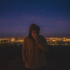 a person standing on top of a hill at night with the city lights in the background