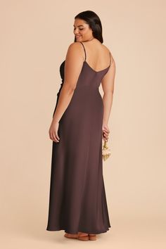 a woman in a long brown dress is looking back at the camera and she has her hand on her hip