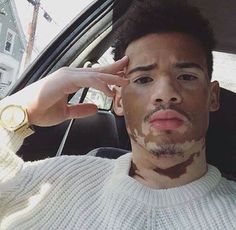 a man with his hand on his head in the back seat of a car while wearing a white sweater