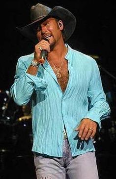 a man in a blue shirt and cowboy hat singing into a microphone while standing on stage