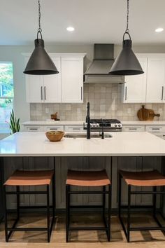 a kitchen island with three stools in front of it and two hanging lights above it