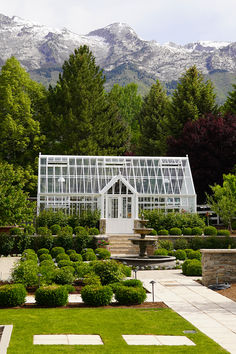 a glass house in the middle of a garden surrounded by trees and bushes with mountains in the background