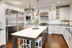 a large kitchen with white cabinets and stainless steel appliances, along with hardwood flooring