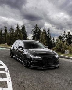 a black car parked on the side of a road next to some trees and bushes