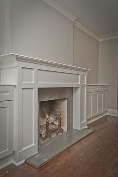 an empty living room with a fire place and white painted fireplace mantels on either side