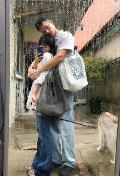 a man and woman taking a selfie in front of a window with rain falling on them