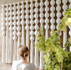 a woman standing in front of a wall hanging with white tassels on it