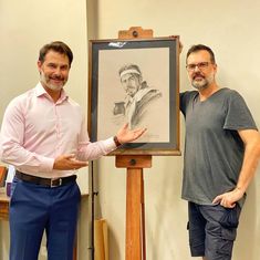 two men standing next to each other in front of a drawing